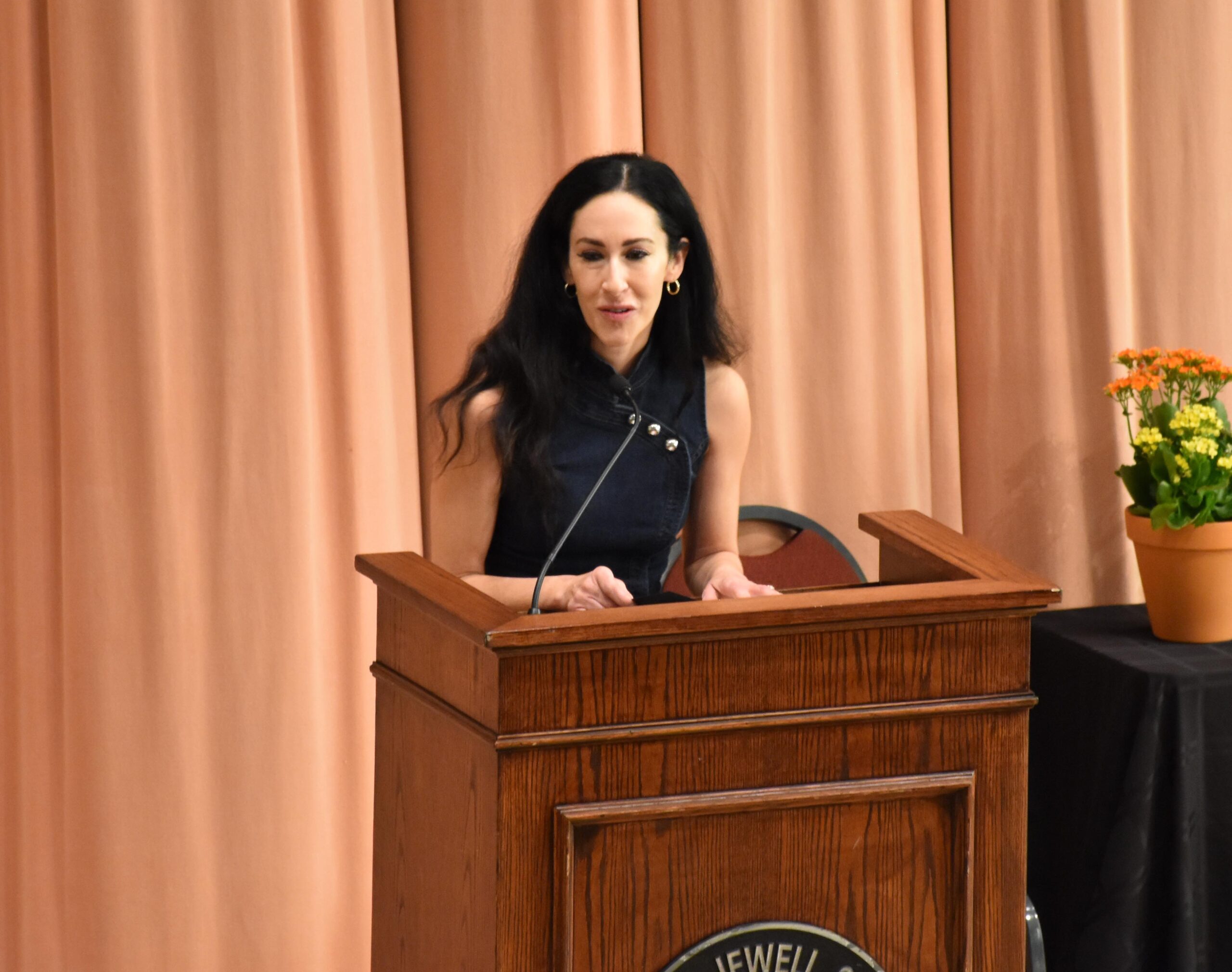 A woman with dark hair standing at a podium speaking to an audience